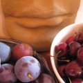 clay sculpture of a chin and mouth with bowls of plums and cherries