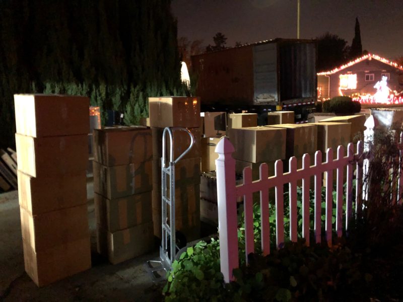 boxes piled in the driveway, container truck and Christmas lights in the background