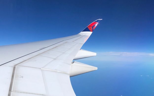 view over an airplane wing with the Delta logo on the wingtip, over the Pacific Ocean