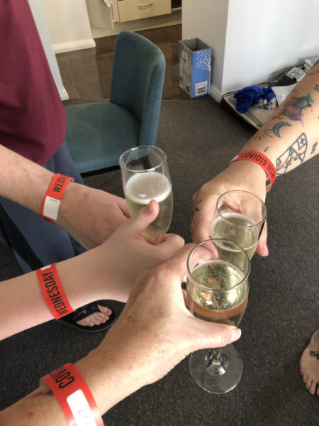 4 arms with wristbands, 3 of them holding glasses of prosecco, one child's hand giving a thumbs up