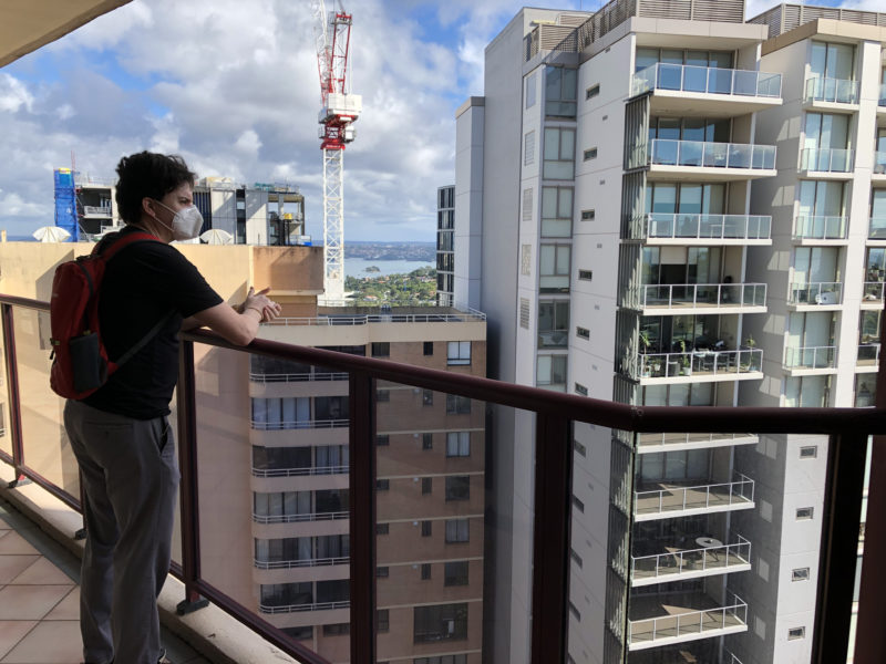 Brendan looking from a balcony high up, with other tall buildings and a crane in the background