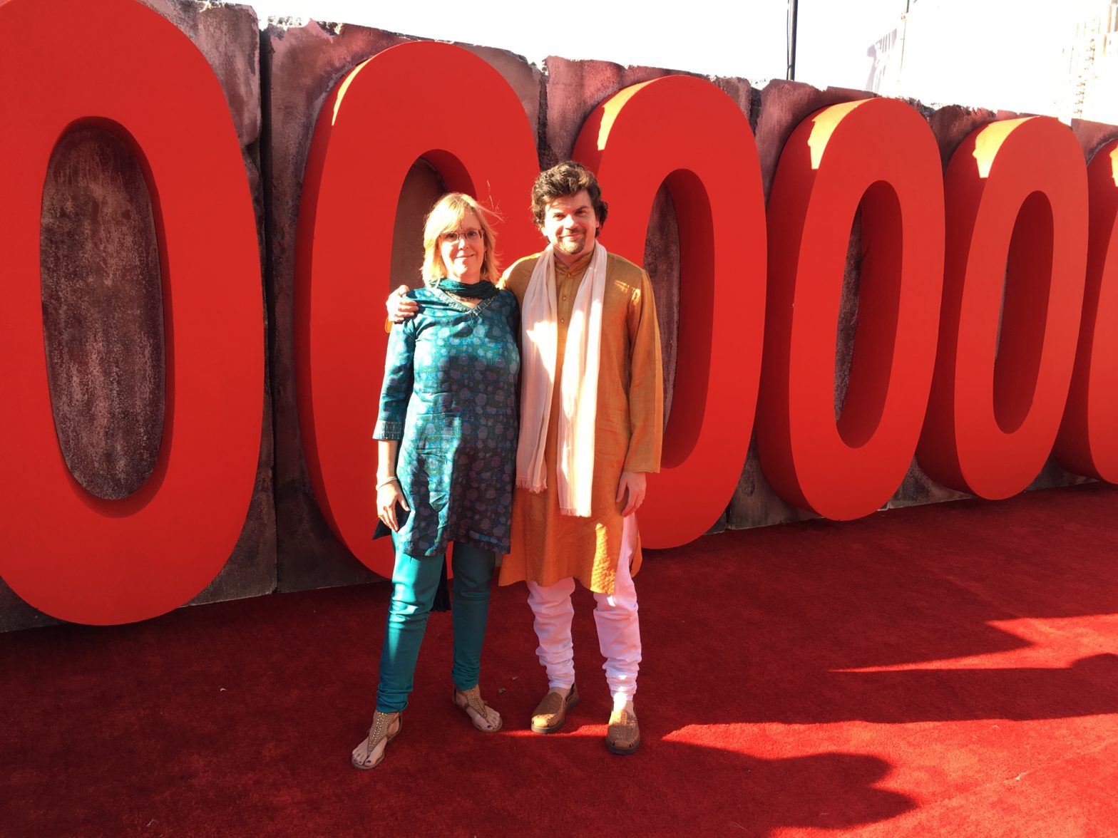 Deirdré and Brendan in front of giant red zeros (part of the 100,00,000 sign)