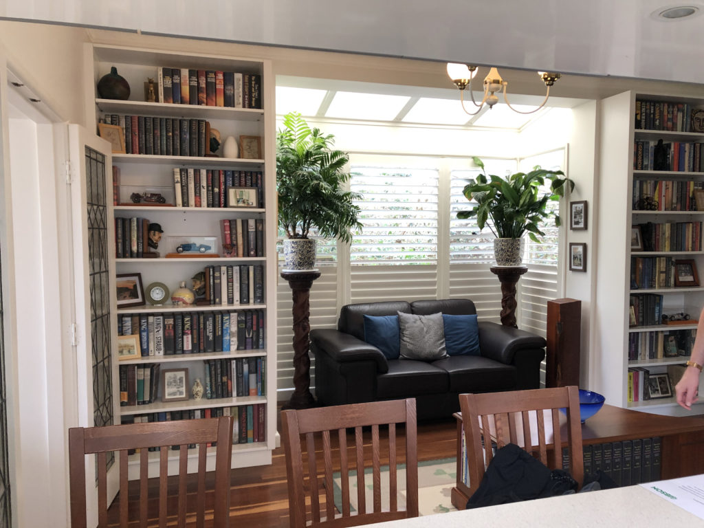 a small sofa in a windowed alcove, flanked by plants on tall stands. The alcove is framed by bookshelves.