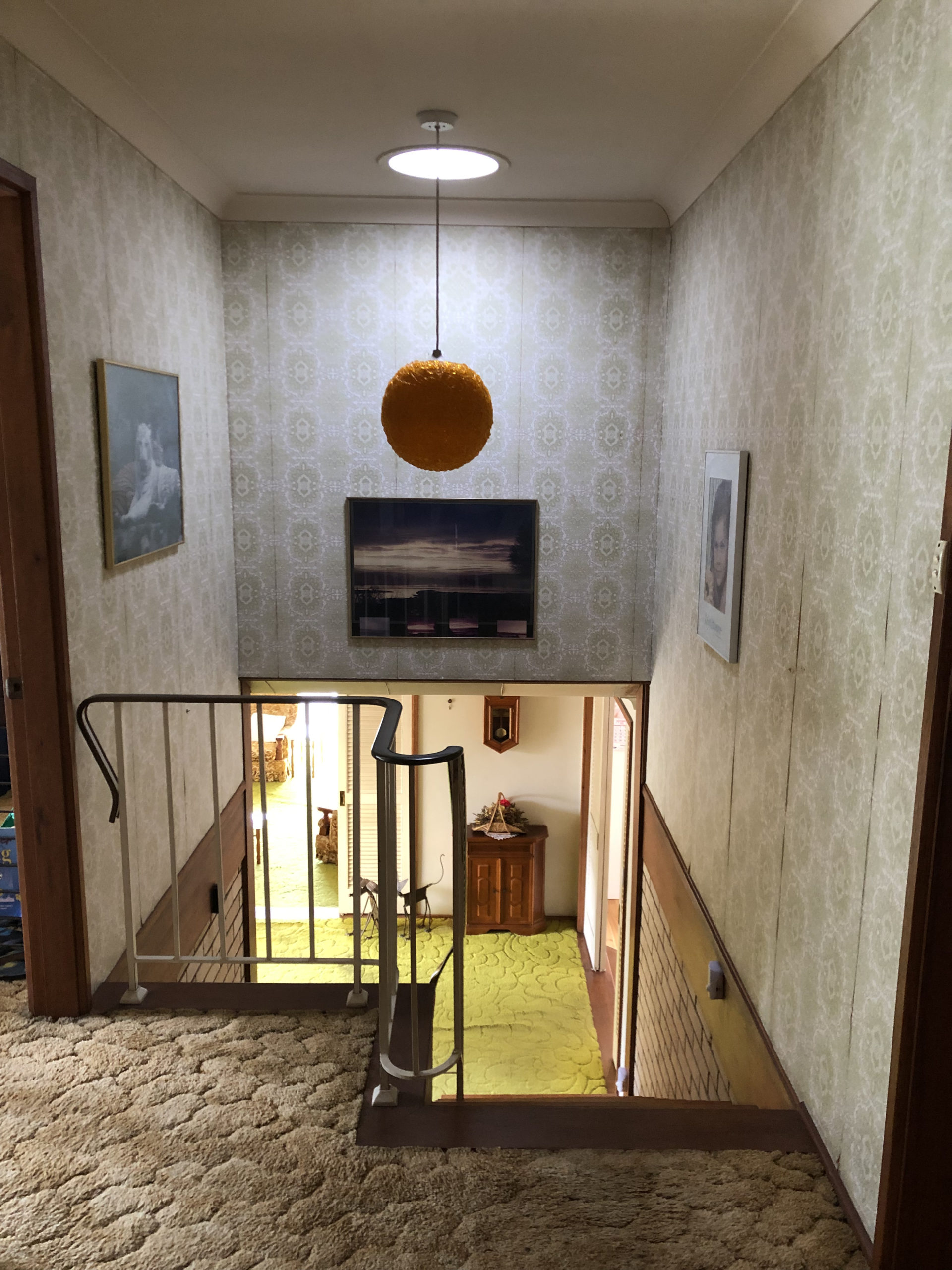 view of upper hallway with a ball lampshade, wallpaper, beige and green carpets