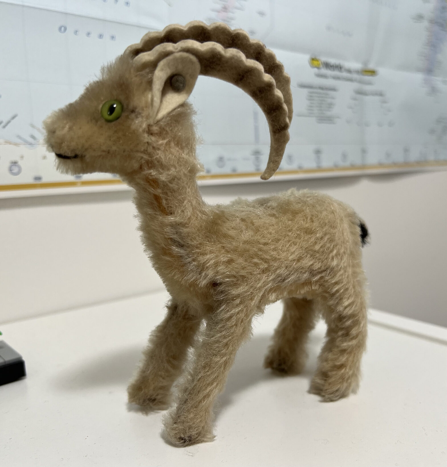 A small stuffed toy ibex with tan fur and felt horns, turned to show the Steiff button in the ear