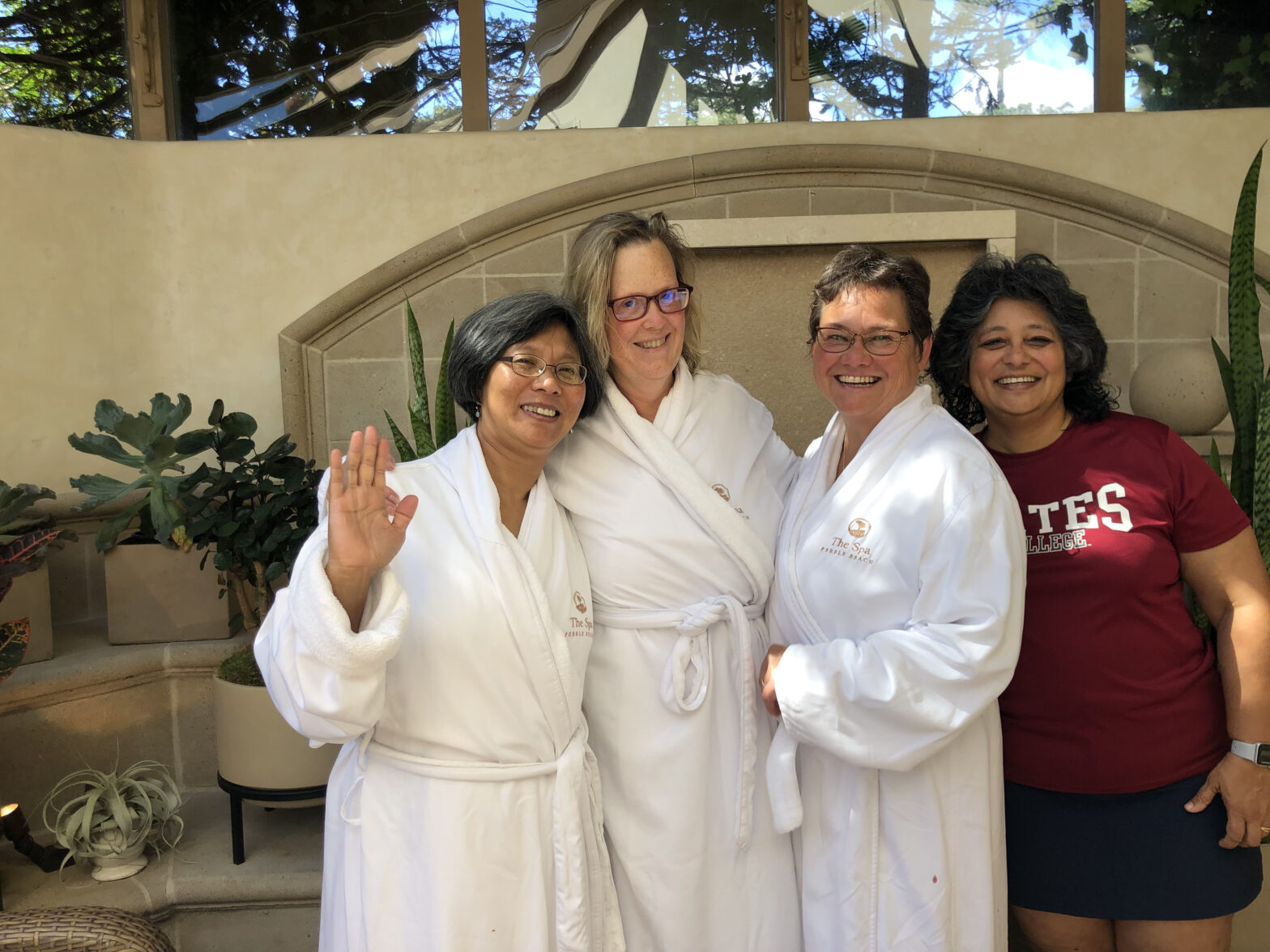 four women, three of them in white bathrobes, stand together smiling