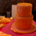 a 2-tiered cake with pink icing decorated with gold paisely patterns