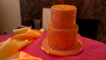 a 2-tiered cake with pink icing decorated with gold paisely patterns