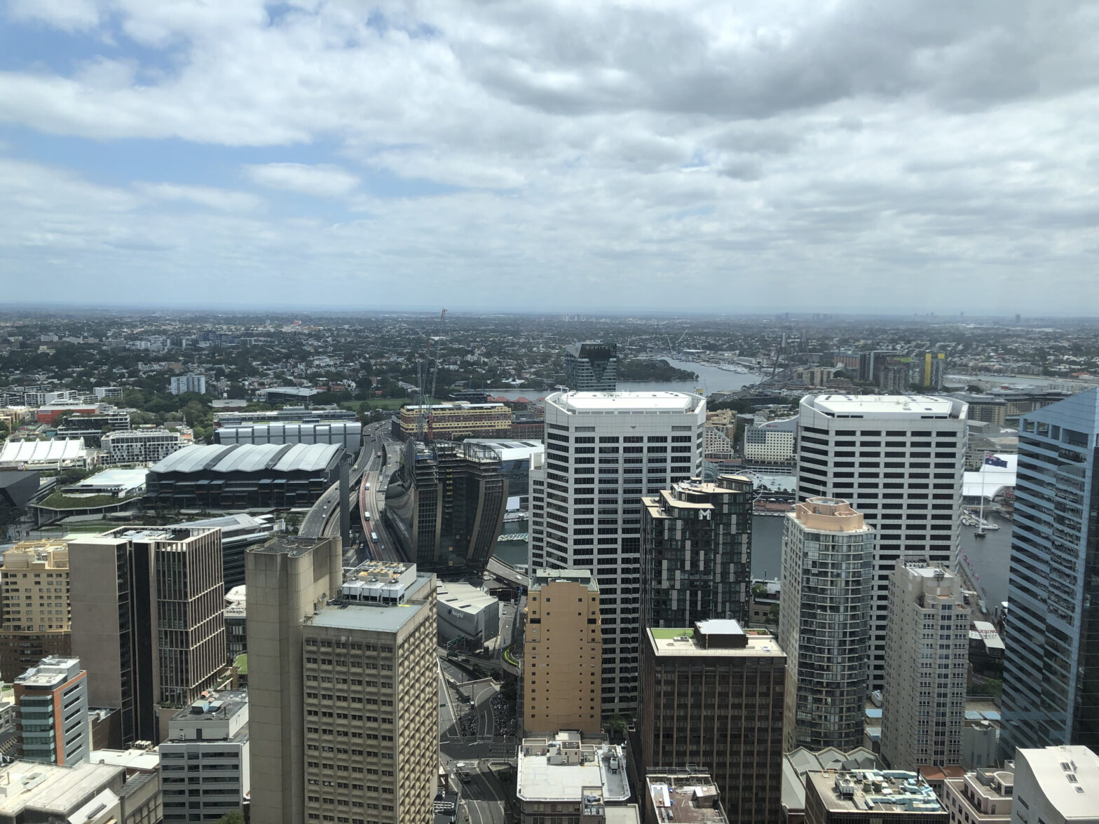 a view from a high floor over tall buildings in downtown Sydney, out to the horizon under a cloudy sky