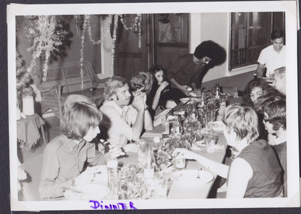 B&W Christmas dinner with a long table of guests. One man has a mustache and is smoking a cigar
